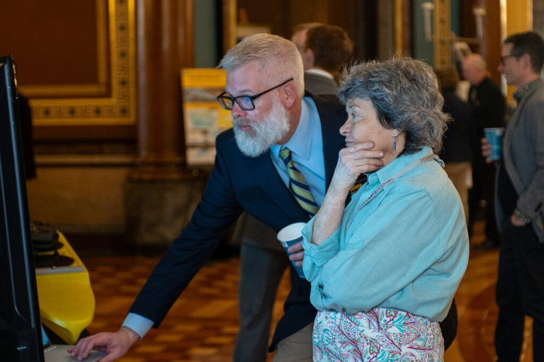 IFC staff Nate Young shows a visitor a model at the Legislative Breakfast event at the Iowa State Capital Rotunda