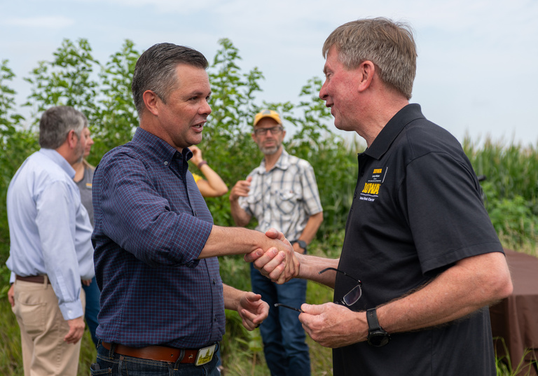Zach Nunn shakes hands with Larry Weber with tall mature corn behind them.