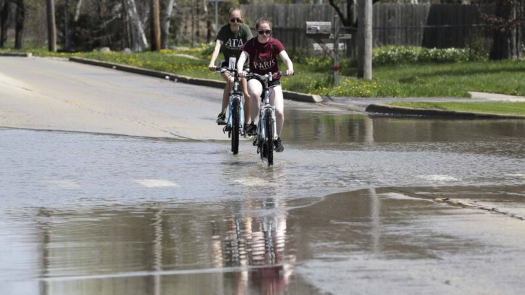 Two people ride bikes in flood water